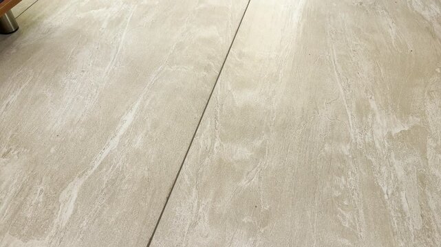 Textured beige ceramic tiles cover an indoor floor surface. The clean, smooth stone pattern brings a pleasant feeling of calm comfort and minimalist peace.