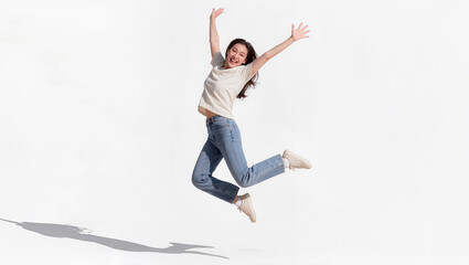 Joyful young Asian woman jumping in mid air with arms raised on white background, freedom and happiness lifestyle concept, editorial portrait photography with copy space