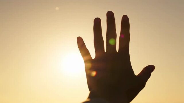 Clean human hand gently rises into an intensely backlit golden hour sky, sunbeams creating warm lens flares and ethereal light shafts through fingers, shallow depth of field with dreamy bokeh.