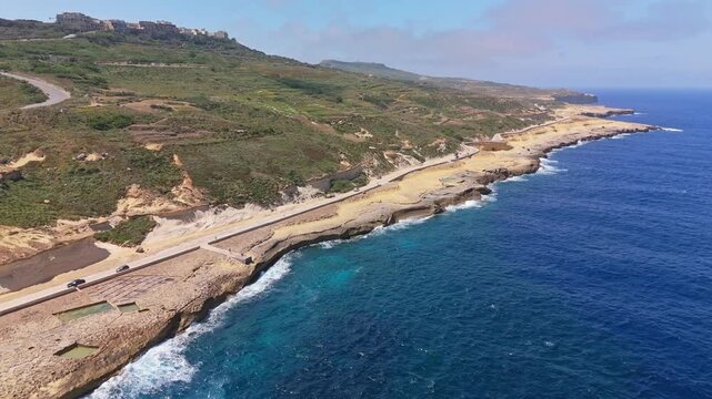 Along Gozo&rsquo;s Xwejni coast, centuries-old salt pans form a stony mosaic above the shimmering Mediterranean, where waves trace Malta&rsquo;s rugged shoreline in a sweeping drone view.