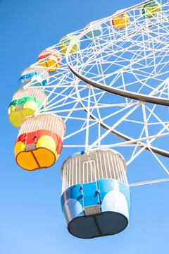 This image showcases a vibrant Ferris wheel set against a clear, brilliant blue sky. The shot captures a low-angle perspective, highlighting the detailed white geometric framework and the colorful pas