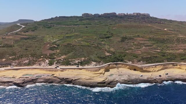 In Xwejni on Gozo, traditional salt pans form geometric patterns along the Mediterranean shoreline, seen from a bird's-eye view during daytime in the rural Maltese landscape.