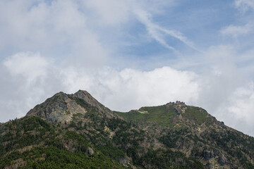 Obraz premium Twin mountain peaks covered with green forest under dramatic cloudy blue sky in Japanese Alps summer landscape