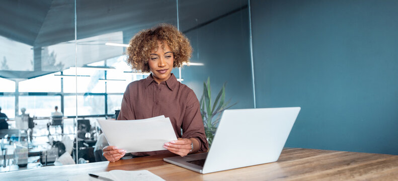 Professional businesswoman entrepreneur reviewing documents at desk with laptop in office. Woman manager executive working reading business paperwork at workspace, doing accounting. Banner, copy space