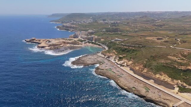 Xwejni salt pans line the rugged coast of Żebbuġ, Gozo, where geometric basins cut into honey-colored rock above the deep blue Mediterranean in a sweeping aerial view.