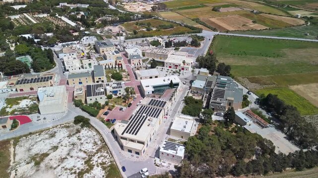In Ta' Qali Crafts Village in Malta, artisan shops and traditional Mediterranean buildings sit among greenery and fields in an outdoor setting captured in an aerial view.