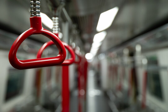 A single red triangular hanging handle in sharp focus inside an MTR train carriage in Hong Kong, with further handles and the empty carriage interior receding into the background