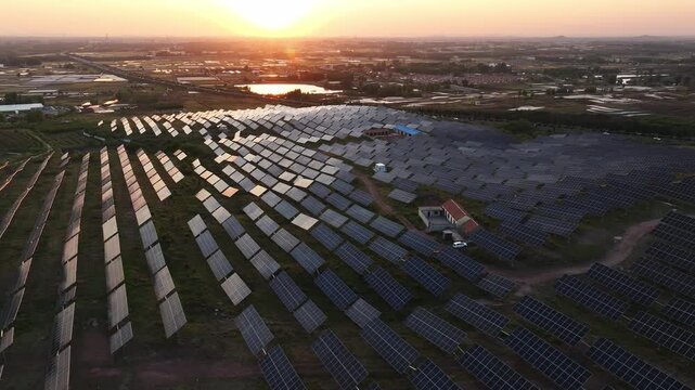 Aerial view of a large-scale photovoltaic power station during sunset with orderly solar panel arrays on rural farmland