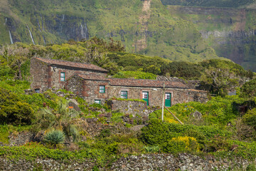 Pintoresca vista de cabañas rústicas de piedra volcánica rodeadas de exuberante vegetación, con espectaculares cascadas fluyendo en la ladera de fondo, Azores. © Maxi Perez