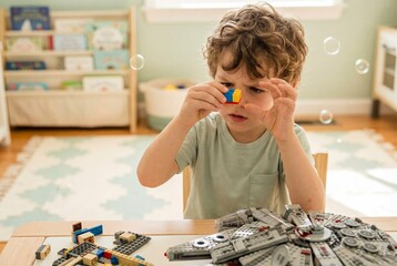 Naklejka premium Focused young boy building a toy spaceship at a sunlit desk.