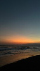 Obraz premium Calm beach at dusk with fading sunlight and soft darkening sky over ocean waves