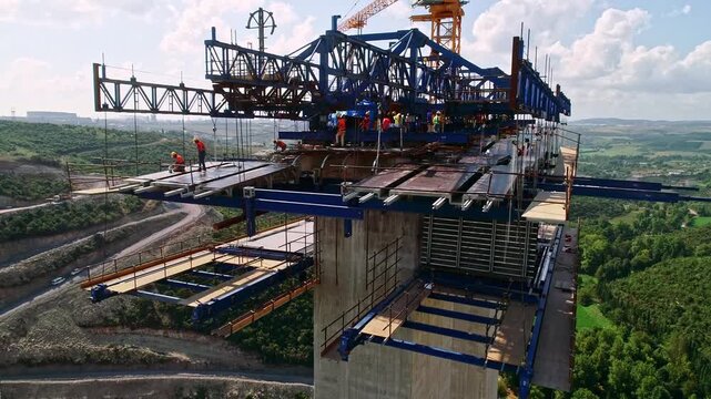 Workers build a viaduct deck with a blue gantry system above a green valley, highlighting bridge construction, safety gear, crane operations, highway infrastructure and civil engineering progress.