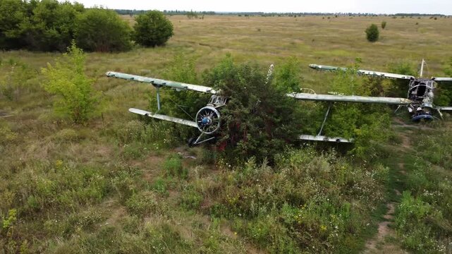 Drone arc shot of weathered An-2 airplane abandoned in overgrown airfield, aviation remains in greenery