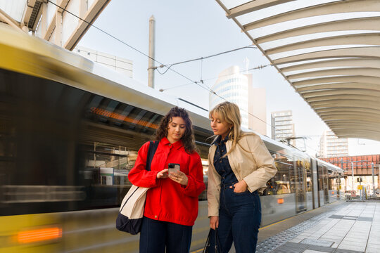 Two Friends Using Phone at the Train Station 