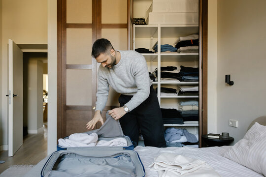 Man Packing Clothes in a Suitcase for Travel in a Bedroom at Home
