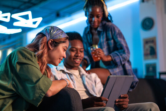 Friends gather, illuminated by neon, sharing a digital tablet screen
