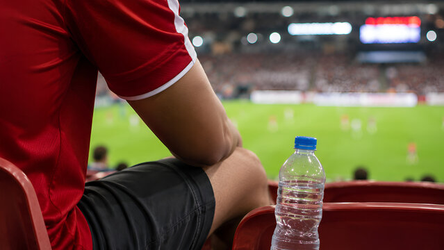 Close Up Partial View of Football Spectator in Red Jersey with Mineral Water Bottle on Stadium Seat
