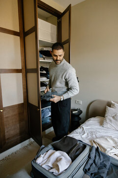 Man Packs Clothes Into Suitcase in Bedroom for Trip