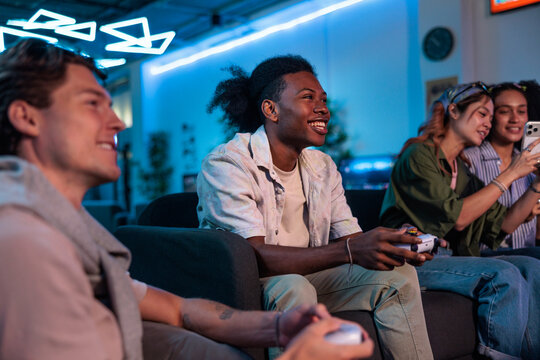 Friends gaming and using phone in a neon-lit room.