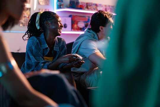 Friends laughing and playing video games in a neon-lit room.