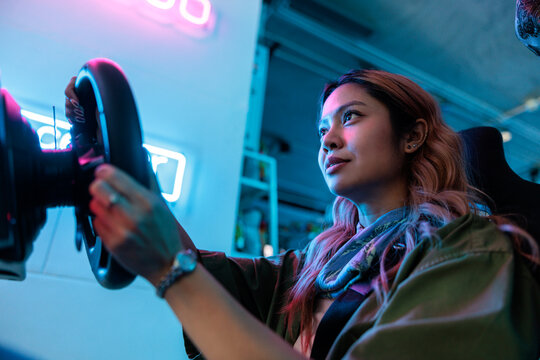 Woman plays racing game under neon lights.