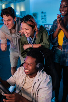 Friends cheer on gamer in blue-lit room.