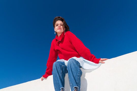 Woman in red sweater sitting on parapet against blue sky