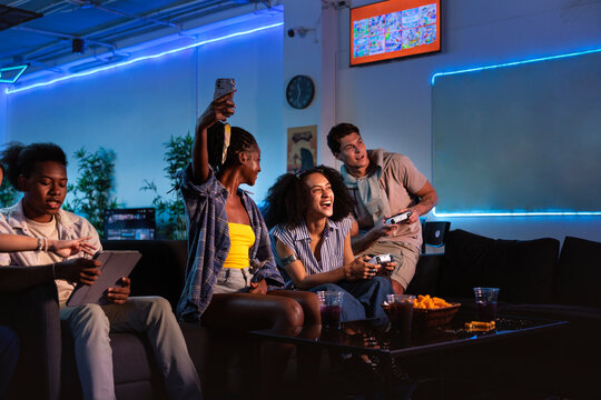 Friends gaming, snacking, and taking photos in a neon room.