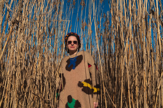 Woman in patterned sweater and sunglasses standing in tall dry reeds
