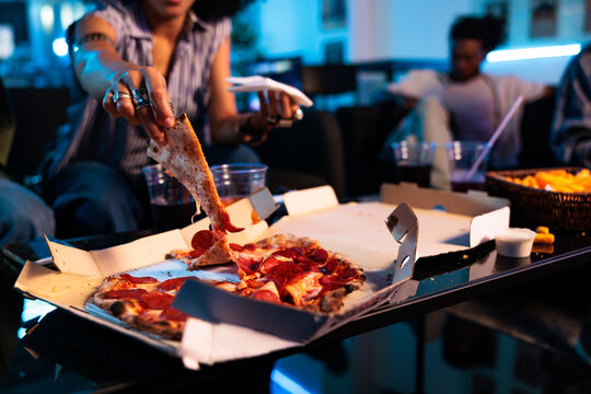 Friends sharing pizza and fries in a blue-lit room.