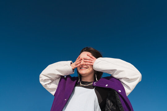 Person covering eyes with hands under bright sun in blue sky