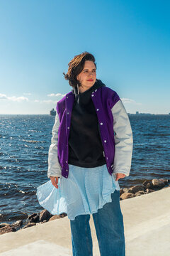 Woman standing by sea in purple varsity jacket
