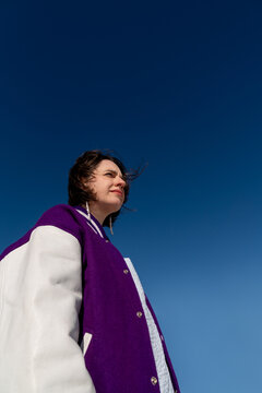 Woman in purple varsity jacket looking away under blue sky