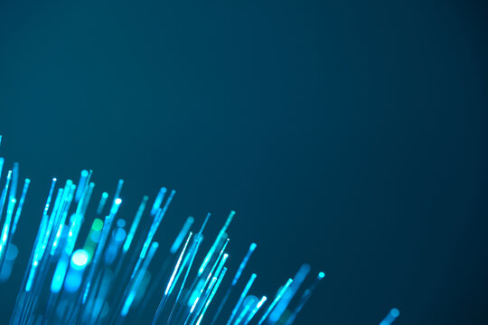 Glowing cyan fiber optic strands abstractly arc across sleek, modern deep teal background.