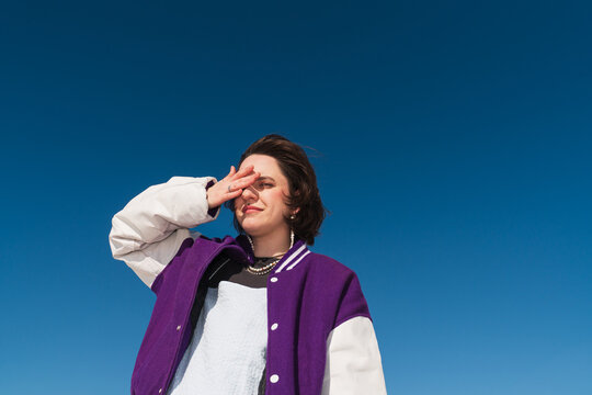 Person shielding eyes in sun wearing purple varsity jacket