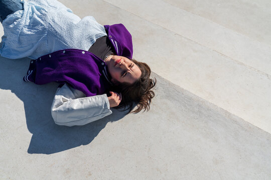 Woman in purple jacket lying on concrete surface looking at camera