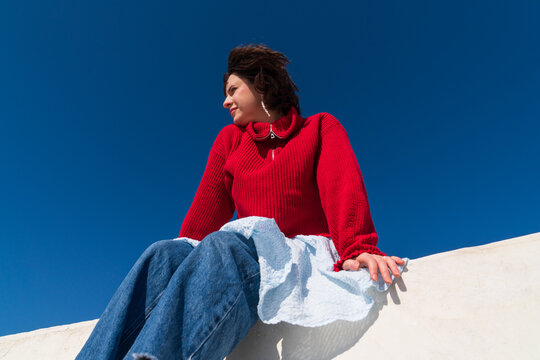 Woman in red sweater sitting on parapet looking aside