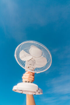 Hand holding white electric fan against blue sky