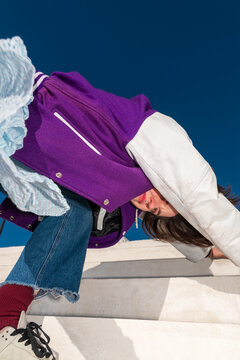 Woman in purple jacket bending over concrete steps under blue sky
