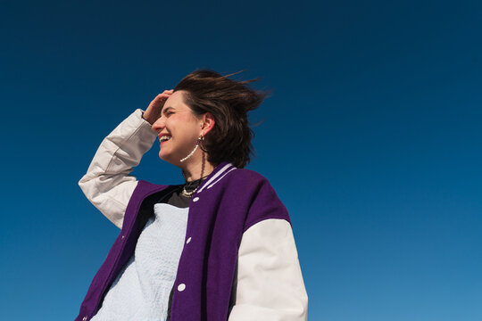 Smiling woman in purple jacket looking away under blue sky