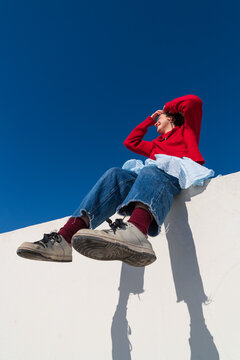Woman in red sweater sitting on wall shielding eyes