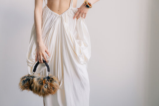 Luxury fashion detail with draped white dress and fur handbag