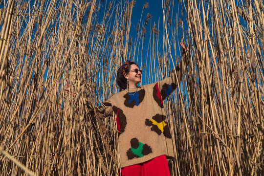 Smiling woman in patterned sweater standing among tall dry reeds