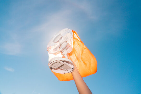 Hand holding electric fan with orange plastic bag outdoors