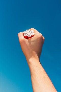 Hand holding multiple alkaline batteries against blue sky