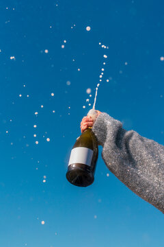Hand holding champagne bottle with blank label and spray