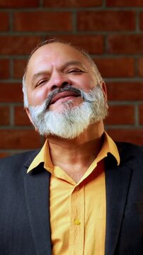 Indian senior businessman flaunting a fan of five hundred rupee notes to the camera with joy and success while standing against a red brick wall in a cozy office with professional moody lighting