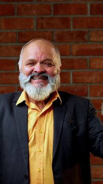 Indian senior businessman flaunting a fan of five hundred rupee notes to the camera with joy and success while standing against a red brick wall in a cozy office with professional moody lighting