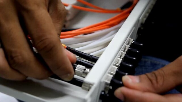 Technician connecting fiber optic cables to a patch panel in a server room
