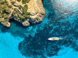 Naklejka premium Aerial view of luxury motor boat yacht in turquoise sea water in Mallorca, Balearic island, Spain. Speedboat moving near rocky cliff coast. Drone summer landscape. Cruise. Top down view. Travel